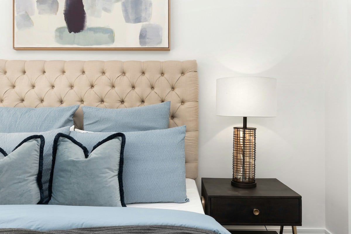 Light blue bed linens on a bed with tufted headboard, nightstand, and lamp