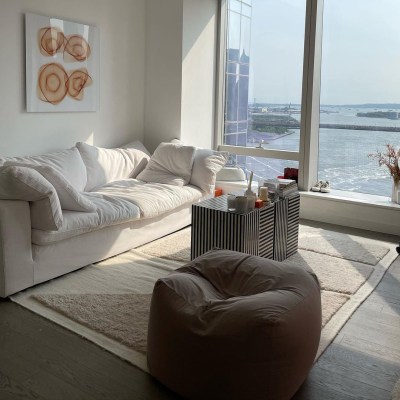 Sipping My Cosmo's apartment overlooking the water featuring a plush white secondhand sofa, a brown ottoman, a tan rug, and a black and white striped coffee table.